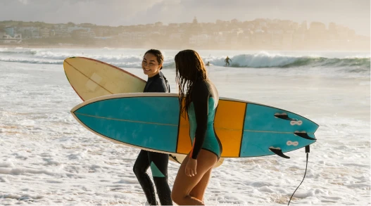 two women walking into the ocean with surfboards